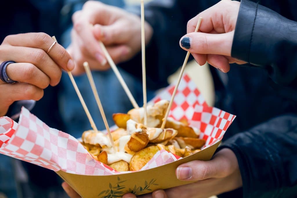 Group of friends visiting and eating poutine at market - Photo: Nenetus